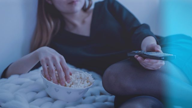 A woman having popcorn and watching TV.