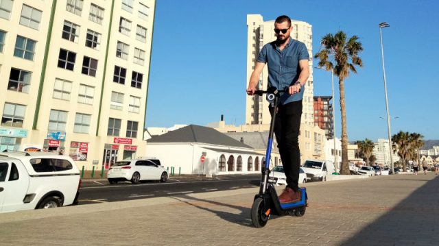 A young man riding an electric kick scooter on Strand promenade, South Africa