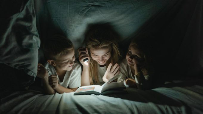 Eurolux Rechargeable 3W LED Emergency Light – Review A women holding a torch, reading to a boy and girl while under a sheet.