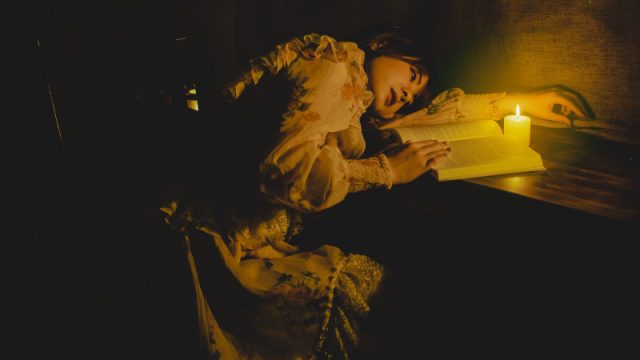 A beautiful woman reading a book by candlelight.